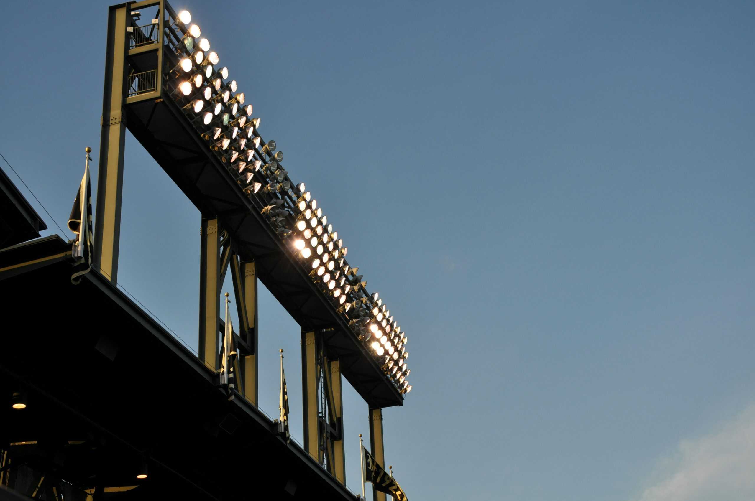 View of powerful stadium lights in Texas mounted on a tall structure, illuminating the sports field below during twilight, with the clear sky providing a serene backdrop.