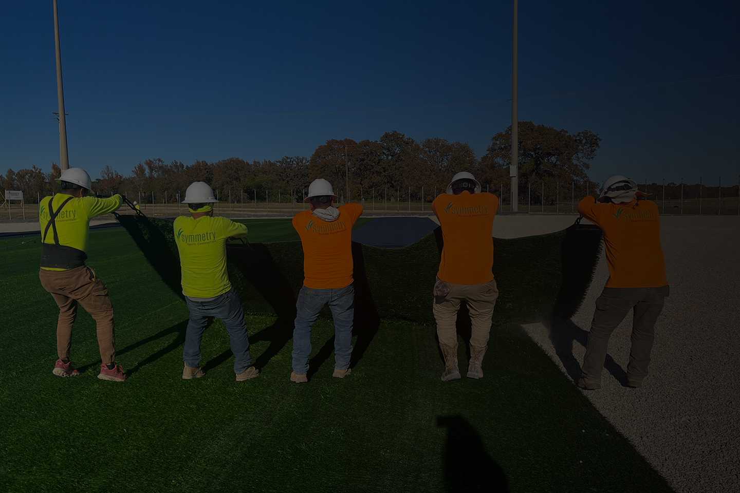 Team of workers installing and maintaining artificial turf on a sports field, ensuring optimal quality and performance.