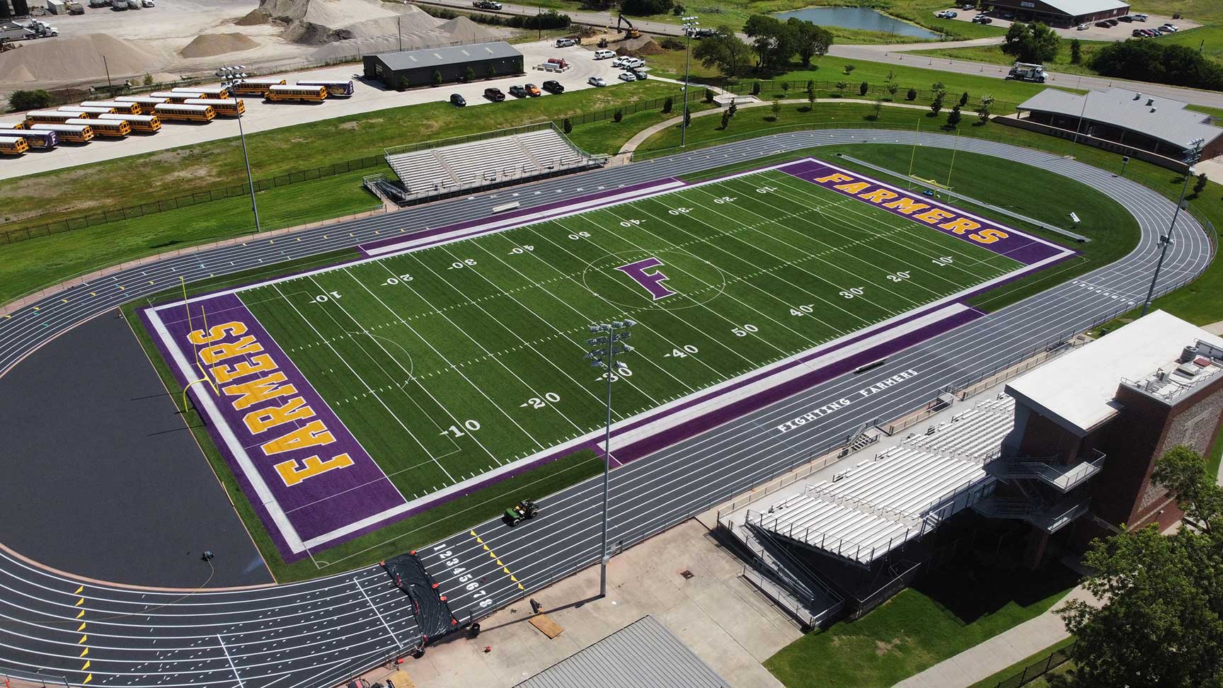 Aerial view of a football stadium with purple end zones reading farmers and a large central f logo on green turf, surrounded by a running track.